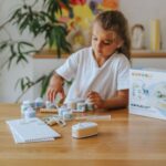 Kit eléctrico Kidyelec de Kidywolf: niña montando un circuito en la mesa junto a la caja de iniciación