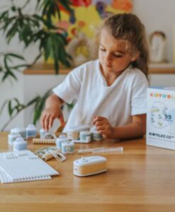 Kit eléctrico Kidyelec de Kidywolf: niña montando un circuito en la mesa junto a la caja de iniciación