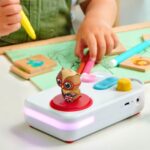 A child's hand holding a marker next to the FABA+ storyteller and the Olivia the Owl figure in English