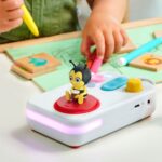 La mano di un bambino con un pennarello accanto al narratore FABA+ con l’ape delle canzoni in catalano