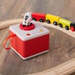 Cuentacuentos infantil FABA rojo con la vaca, sobre suelo de madera junto a un tren de juguete