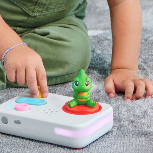 A child's hands pressing the buttons on the FABA+ story-telling device, with the emotions chameleon sitting on top of it