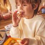 Pack de 3 cajas de almuerzo apilables: niño comiendo un palito de pan con fruta en una caja naranja