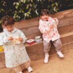 Pack de 3 cajas de almuerzo apilables: dos niños con chubasquero merendando en un banco de madera con sus cajas