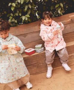 Pack de 3 cajas de almuerzo apilables: dos niños con chubasquero merendando en un banco de madera con sus cajas