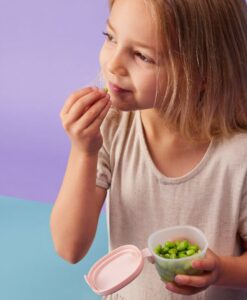 Niña comiendo de un depósito hermético b.box abierto, con la tapa colgando de la bisagra