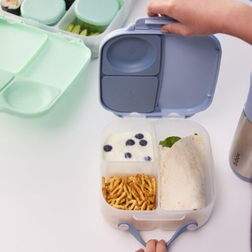 Manos colocando la comida en los compartimentos de la fiambrera infantil b.box