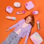 Niña alrededor de productos b-box con fondo naranja y botellas y tuppers de color rosa