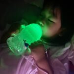 Niña bebiendo por la pajita del vaso b.box mientras el vaso brilla en la penumbra