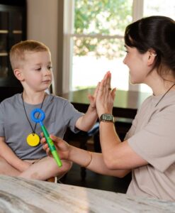 Niño chocando la mano con su terapeuta mientras sujeta un Z-Vibe Plus verde con el cabezal Circle azul