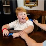 Niño con el cabezal Hex naranja junto a la boca, montado en un mango azul, mientras una adulta le sujeta la mano