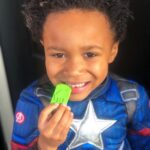 Niño disfrazado de superhéroe que sonríe con el colgante Fantasma verde del collar mordedor en la mano