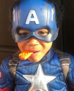 Niño disfrazado de superhéroe mordiendo el colgante Calabaza amarillo de su collar mordedor