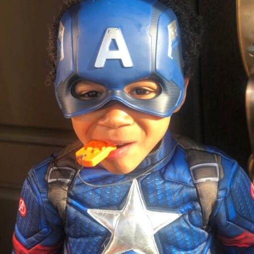 Niño disfrazado de superhéroe mordiendo el colgante Calabaza amarillo de su collar mordedor