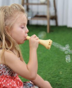 Solución Touchable Bubbles de Mother's Corn: niña soplando pompas con una trompeta en el césped
