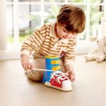 Zapatilla Tie-It de Hape: niño sentado en el suelo practicando con los cordones, para aprender a atar los cordones