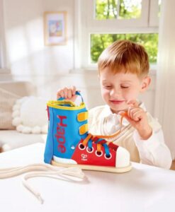 Zapatilla Tie-It de Hape: niño atando los cordones de la zapatilla en la mesa, para aprender a atar los cordones
