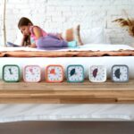 Niña leyendo tumbada en la cama junto a una balda con seis relojes Time Timer MOD Home Edition