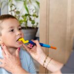 Niño mordiendo el cabezal Zig Zag amarillo de ARK, montado en un Z-Vibe azul que sujeta una adulta