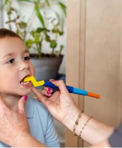Niño mordiendo el cabezal Zig Zag amarillo de ARK, montado en un Z-Vibe azul que sujeta una adulta