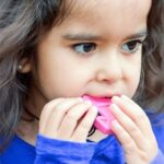 Niña mordiendo el colgante Diamante rosa fucsia mientras lo sujeta con las dos manos
