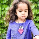 Niña mordiendo el colgante Diamante rosa fucsia mientras lo sujeta con las dos manos