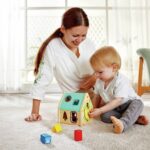 Clasificador Casa de Criaturas de Hape: niño pequeño eligiendo una pieza junto a la casita mientras su madre mira