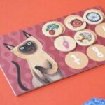 Juego Where are my socks? de Londji: tablero de un gato siamés con fichas de objetos y números