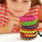 Kidz Maker Pulseras de la amistad de 4M: niña mirando sobre la mesa la torre de pulseras trenzadas que ha hecho