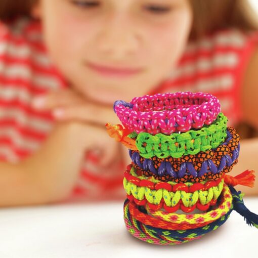 Kidz Maker Pulseras de la amistad de 4M: niña mirando sobre la mesa la torre de pulseras trenzadas que ha hecho