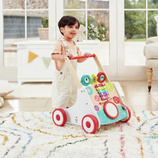 Andador musical de madera de Hape: niño pequeño de pie empujando el andador sobre una alfombra de colores