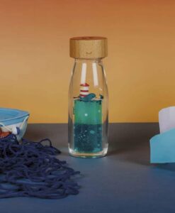 Botella sensorial Ballena de Petit Boum: botella sobre una mesa azul junto a una red y un barco de juguete