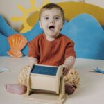 Sensory Roller de Petit Boum: bebé sentado en el suelo girando el rodillo, rodillo sensorial de madera