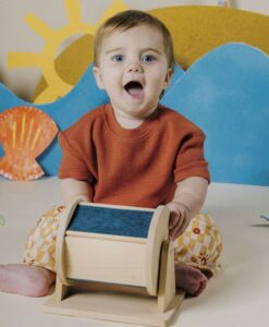 Sensory Roller de Petit Boum: bebé sentado en el suelo girando el rodillo, rodillo sensorial de madera