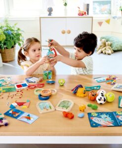 Avocado Fidget de Hape: dos niños jugando en una mesa llena de juguetes de la marca, entre ellos el aguacate