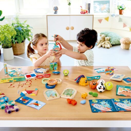 Avocado Fidget de Hape: dos niños jugando en una mesa llena de juguetes de la marca, entre ellos el aguacate