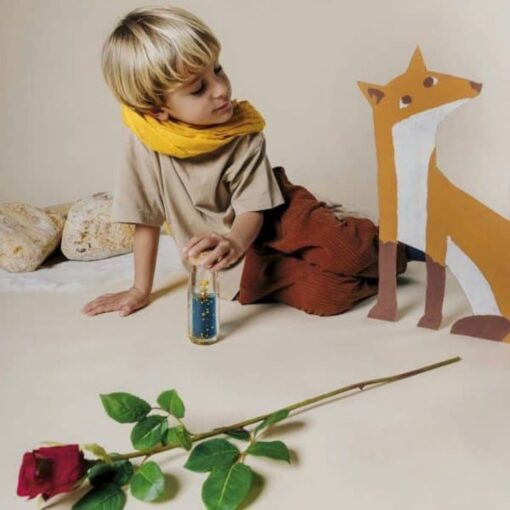 Botella sensorial El Principito de Petit Boum: niño con bufanda amarilla mirando la botella en el suelo