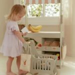 Carrito de la compra de Little Dutch: niña empujando el carrito junto a un puesto de mercado de juguete